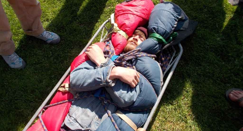 a person lies in a stretcher during a wilderness first responder training